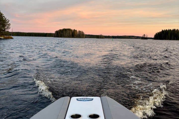 View from boat's stern on lake at sunset with pink sky.