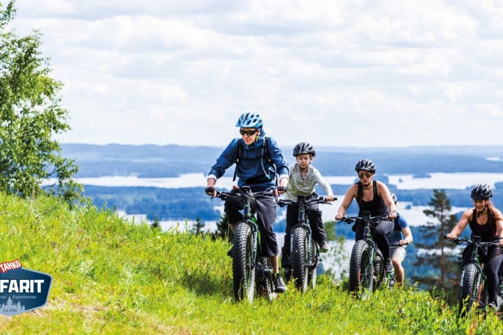 Group of people cycling on a grassy hill with lakes in the background.
