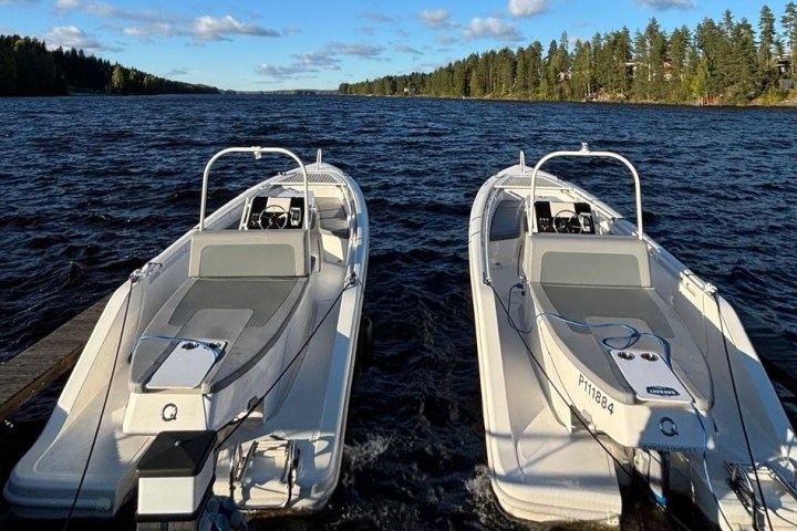Two white boats docked on a lake with forested shores under a blue sky.