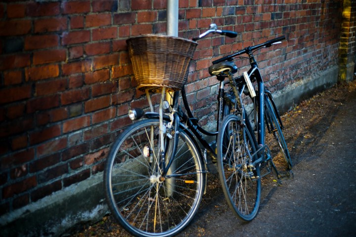 Two bicycles leaning against a brick wall with a basket on one.