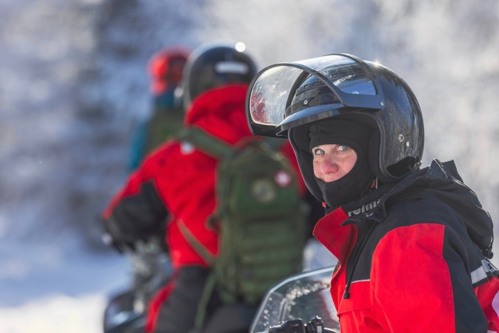 People in red jackets riding snowmobiles in snowy landscape.