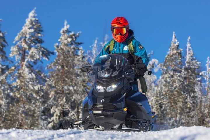 Person in red helmet riding snowmobile in snowy forest.