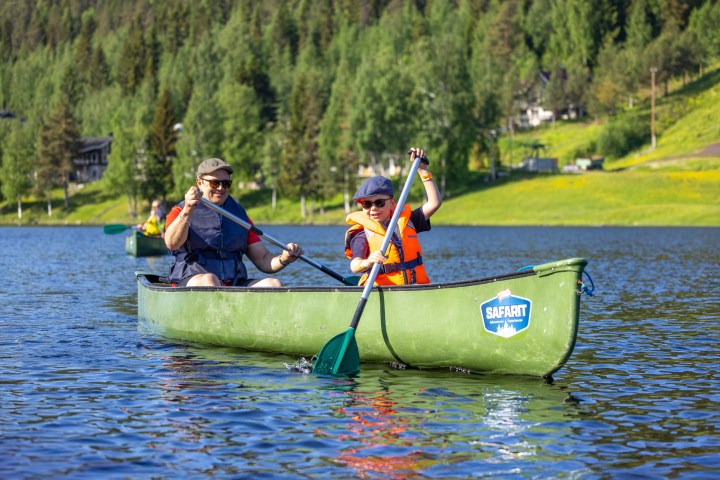 Two people paddling a green canoe on a lake with forested background.