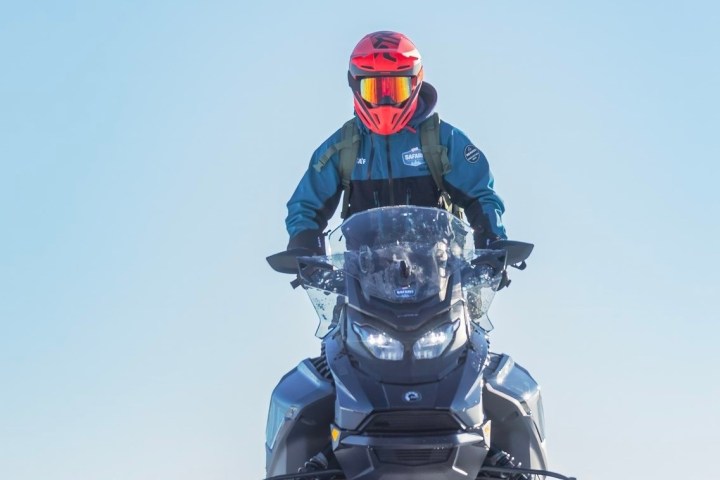 Person in helmet on snowmobile under clear blue sky.