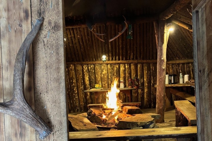 Cozy wooden cabin with a lit fire pit and benches inside.