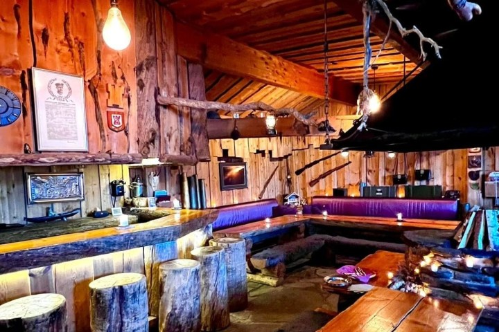 Rustic wooden bar with stools, tables, and dim lighting.
