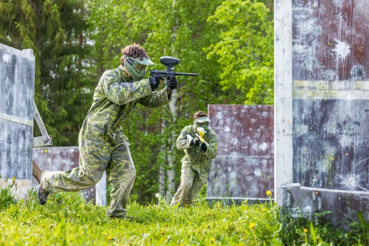 Two people in camouflage gear playing paintball in an outdoor field.