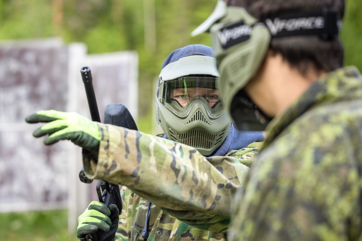 Two people in camouflage gear and masks engaged in outdoor paintball.