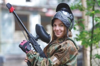 Person in camouflage holding paintball gun, wearing a helmet.