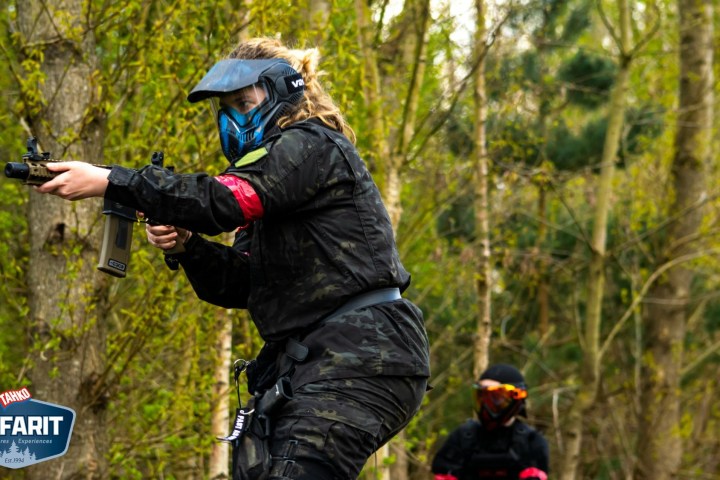 Person in paintball gear aiming a marker in a wooded area.