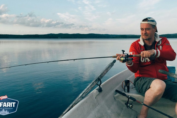 Man fishing on a lake in a small boat, under a cloudy sky.