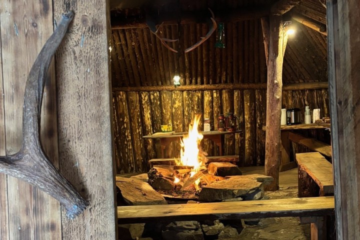 Rustic cabin interior with a central fireplace and wooden benches.