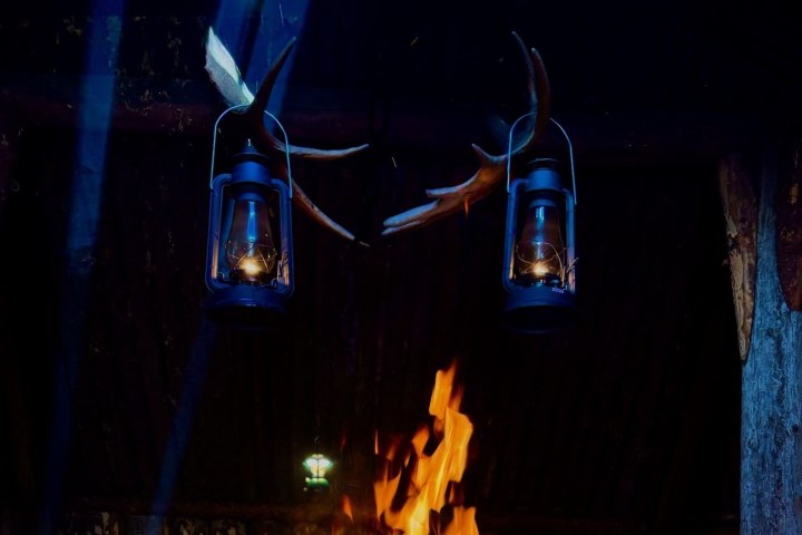 Two lanterns hanging above a lit fire in a dark setting.