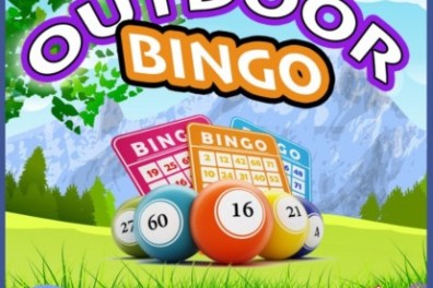 Colorful bingo balls and cards on grass with mountains in background.