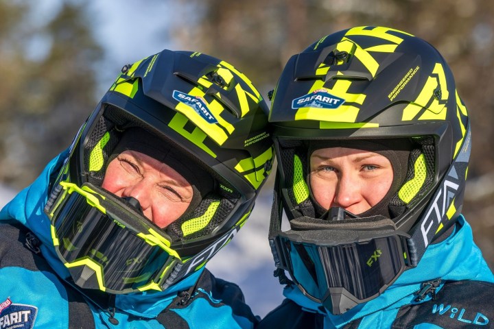 Two people in blue jackets wearing black and yellow helmets outdoors.