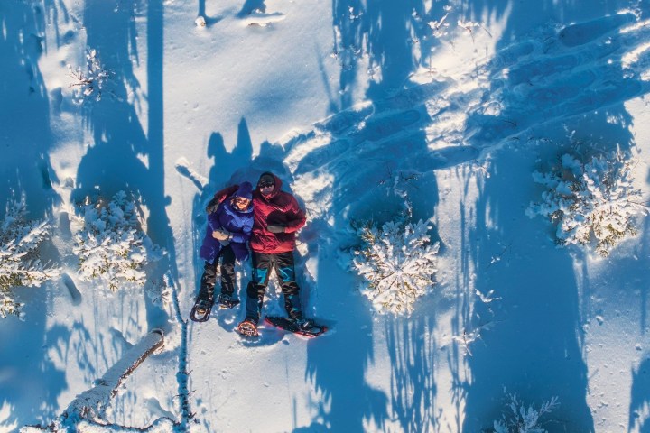 Two people in winter clothing lying on snow with snowshoes nearby.