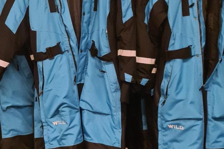 Several blue and black winter suits hanging on a rack indoors.