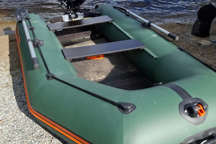 Green inflatable boat with outboard motor on a pebble shore.