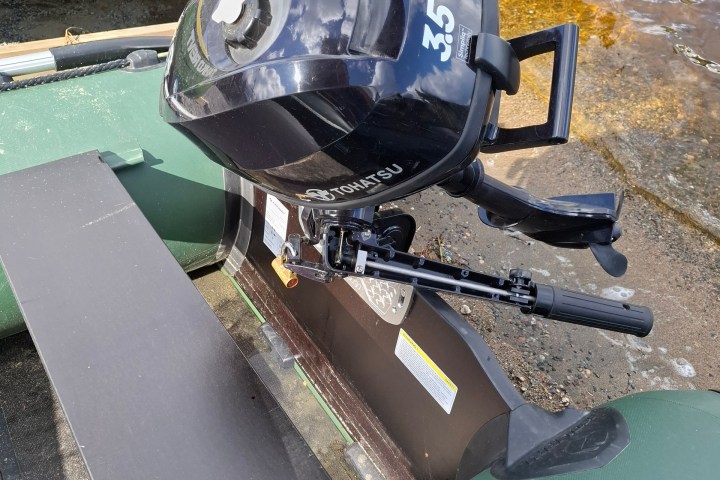 Outboard motor on small boat near water's edge, green canoe in background.