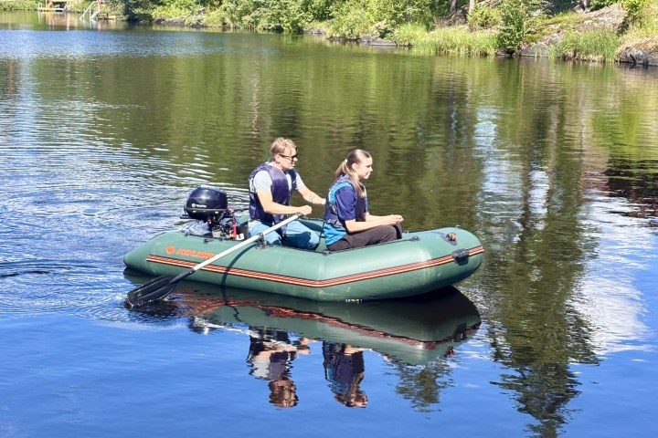 Two people in a small motorized inflatable boat on a calm lake.