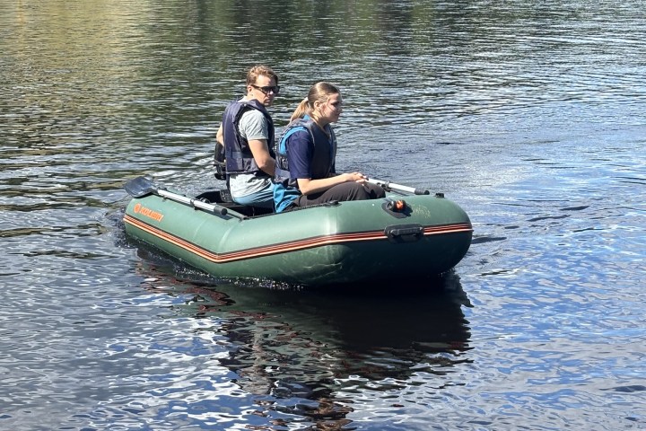 Two people in a green motorboat on a lake with a forested shoreline.