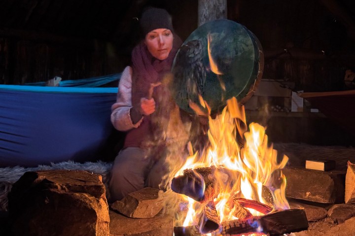 Person by campfire playing drum in a cozy, dimly lit setting.