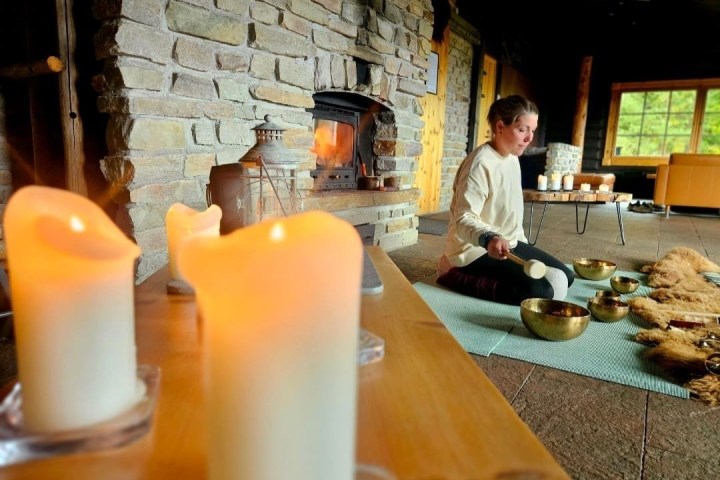Person meditating with singing bowls in a cozy room with lit candles.